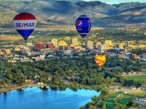 An aerial view of downtown Colorado Springs with three hot air balloons in the sky above Prospect Lake. 